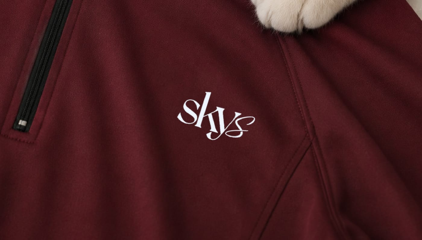 Close-up of the After Sunset half-zip fabric with embroidered skys logo — and an approving cat paw