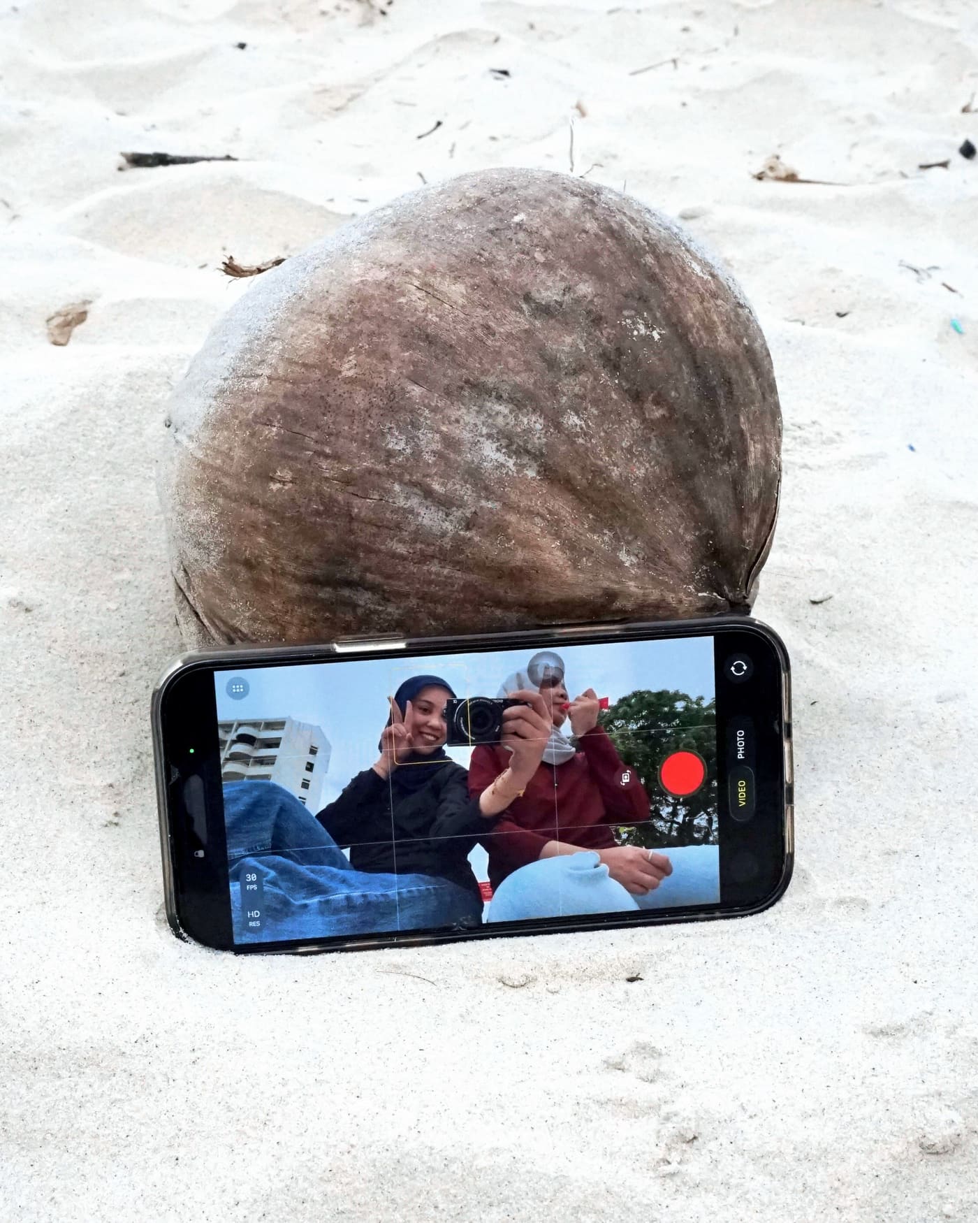 Filming a beach video framed by a coconut on the sand