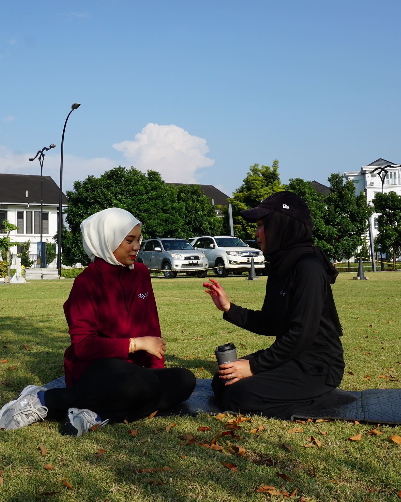 Two friends in Skys half-zips stretching on mats in a park